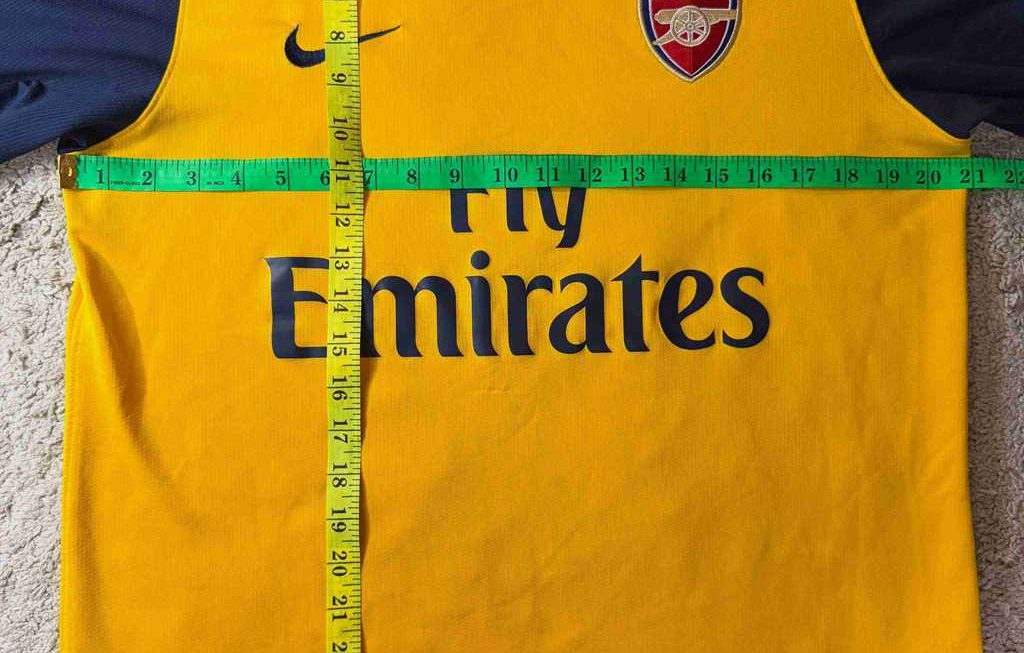 Geel Arsenal voetbalshirt plat opgemeten met meetlinten om de exacte lengte en borstomvang te bepalen